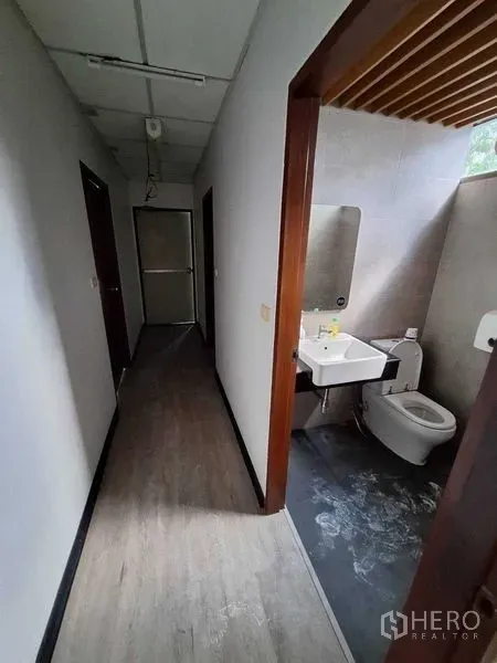 Office Space for rent in Watthana, Bangkok - Restroom with sink, mirror, toilet and gray tiles next to the corridor.