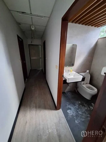 Office Space for rent in Watthana, Bangkok - Restroom with sink, mirror, toilet and gray tiles next to the corridor.