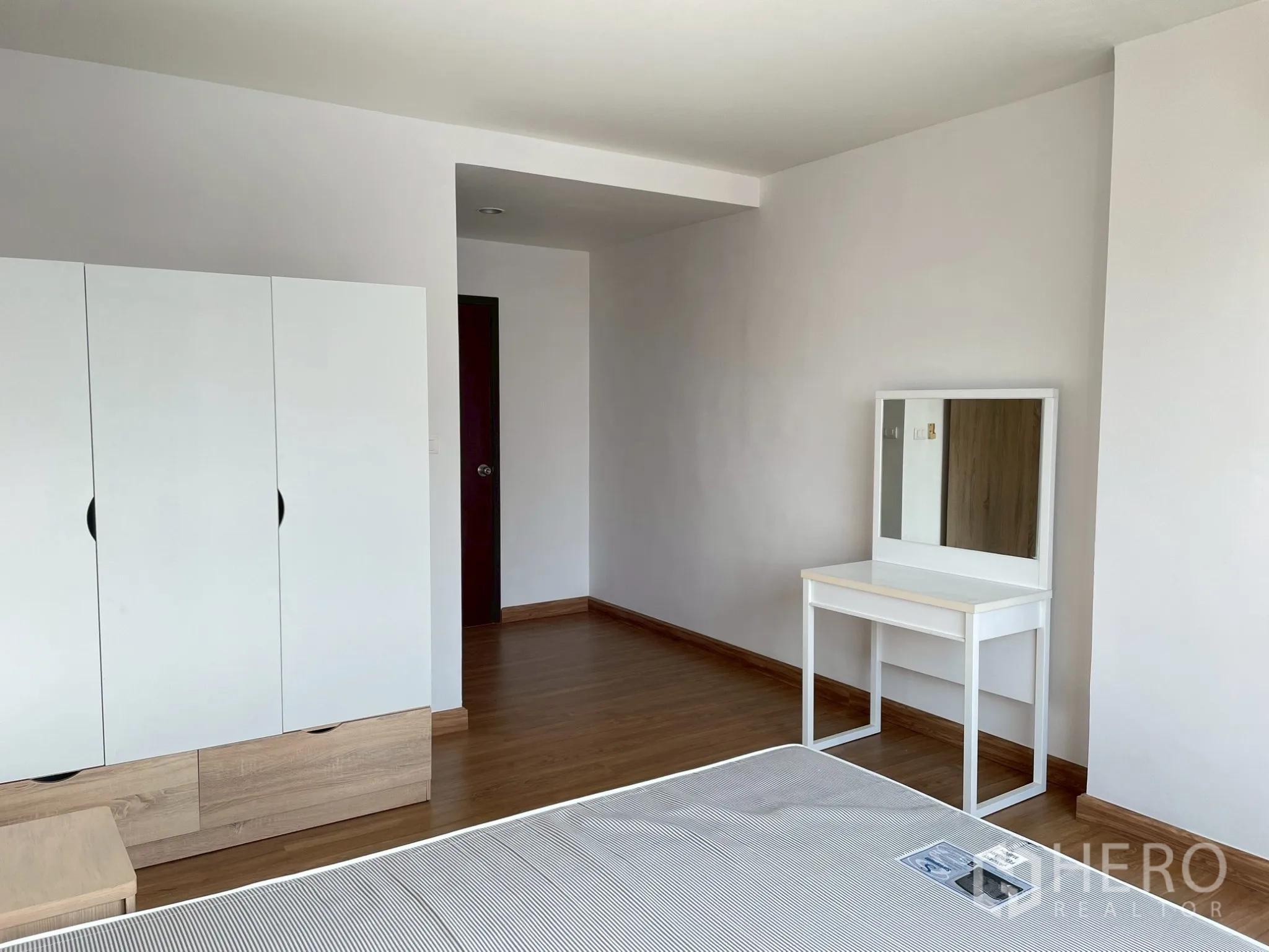 Apartment for rent in Khlong Toei, Bangkok - Bedroom with wardrobe, bedside table, and white dressing table with mirror.