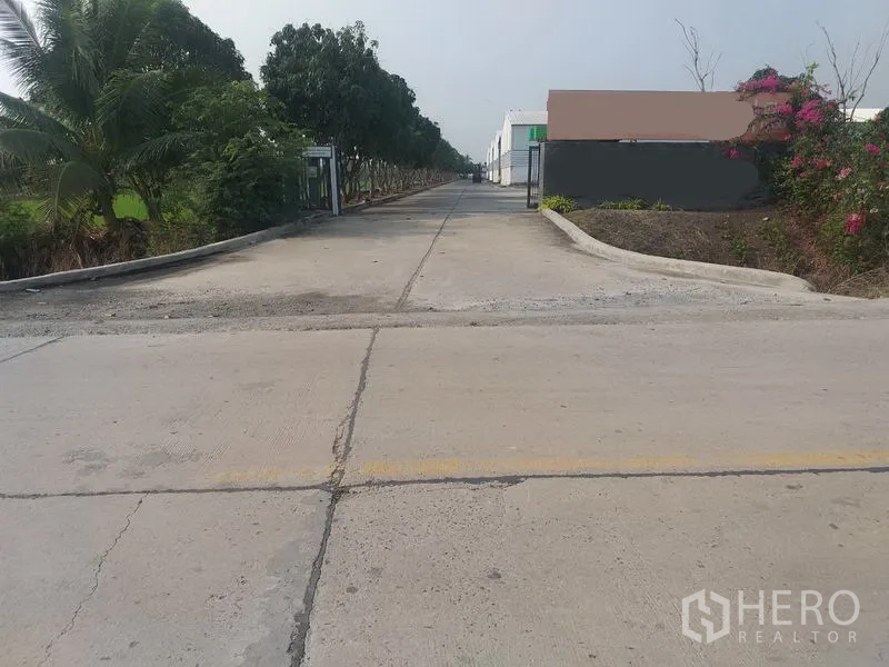 Warehouse for rent in Pathum Thani - Gated entrance to the warehouse compound with a long, tree-lined approach.