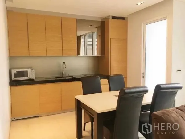 Condominium for rent in Bang Rak, Bangkok - Modern light wood kitchen with built-in cabinets, microwave, and four-seat dining table.