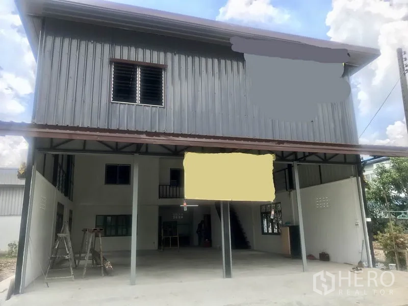 Warehouse for rent in Lam Luk Ka, Pathum Thani - Two-storey steel-clad warehouse exterior with covered loading bay and front parking.