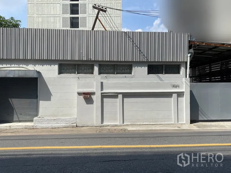 Warehouse for rent in Chatuchak, Bangkok - Street‑facing facade of a single‑story warehouse with high corrugated parapet and narrow windows.