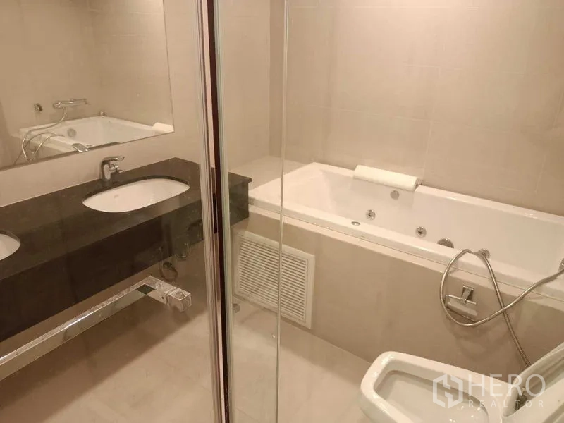 Condominium for rent or sale in Huai Khwang, Bangkok - Bathroom with jetted bathtub, glass shower screen and long vanity.