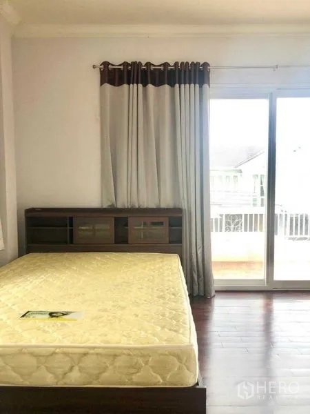 บ้าน ขายในLat Krabang, Bangkok - ห้องนอนรับแสงธรรมชาติ พื้นไม้เข้ม พร้อมประตูระเบียงและหัวเตียงบิวท์อิน