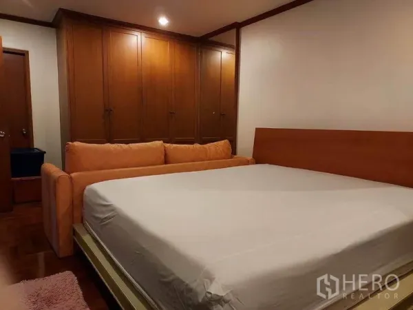 Condominium for rent or sale in Watthana, Bangkok - Master bedroom with king bed, orange sofa and a wall of wooden wardrobes in an Ekkamai condo.