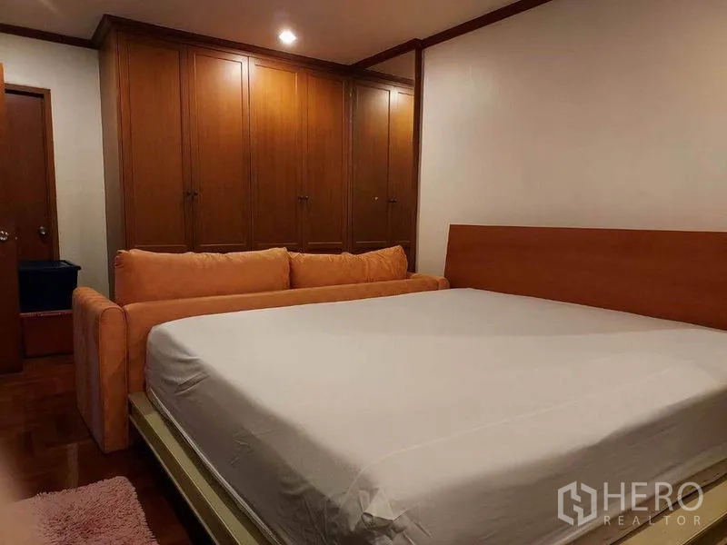 Condominium for rent or sale in Watthana, Bangkok - Master bedroom with king bed, orange sofa and a wall of wooden wardrobes in an Ekkamai condo.