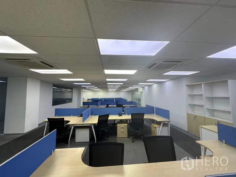 สำนักงาน ให้เช่า - โซนทำงานร่วมกัน โต๊ะรูปตัวแอล ฉากกั้นสีน้ำเงิน และชั้นวางของติดผนัง