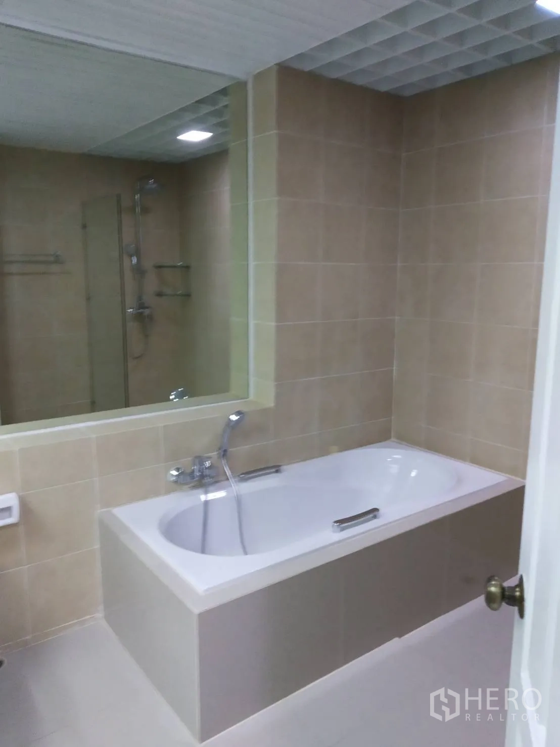 Condominium for rent in Pathum Wan, Bangkok - Tiled bathroom with a built-in bathtub, handheld shower and wide wall mirror.