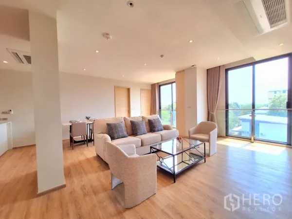 อพาร์ทเมนท์ ให้เช่าในBang Na, Bangkok - ห้องนั่งเล่นมุม โซฟาโทนกลาง ประตูระเบียง และแปลนเปิดโปร่ง