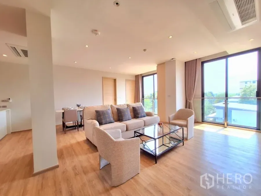 อพาร์ทเมนท์ ให้เช่าในBang Na, Bangkok - ห้องนั่งเล่นมุม โซฟาโทนกลาง ประตูระเบียง และแปลนเปิดโปร่ง