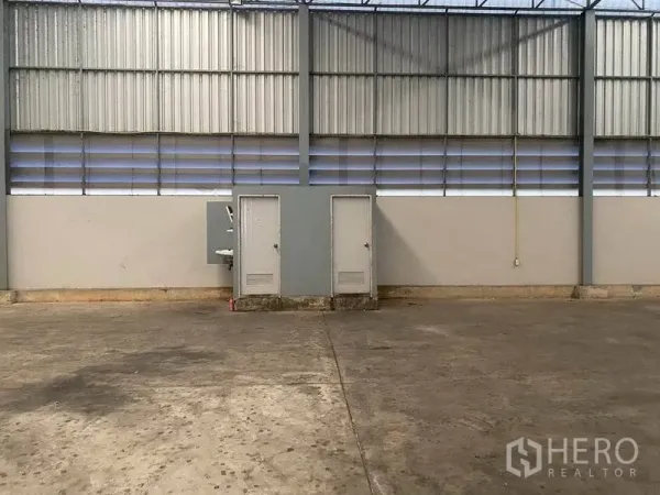 Warehouse for rent in Lat Krabang, Bangkok - Warehouse wall with ventilation louvres, two utility doors and a sink on the concrete floor.
