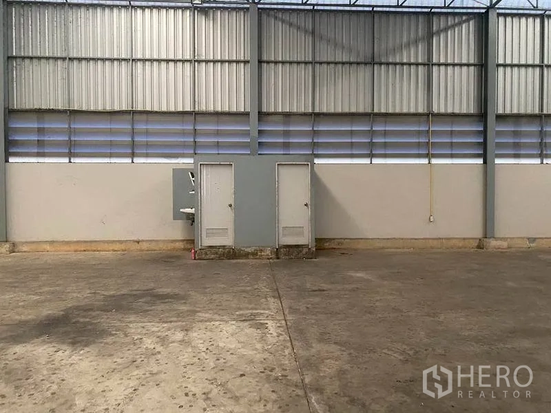 Warehouse for rent in Lat Krabang, Bangkok - Warehouse wall with ventilation louvres, two utility doors and a sink on the concrete floor.