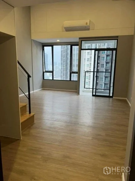 Condominium for sale in Huai Khwang, Bangkok - Sunlit living area with floor-to-ceiling windows and balcony door.