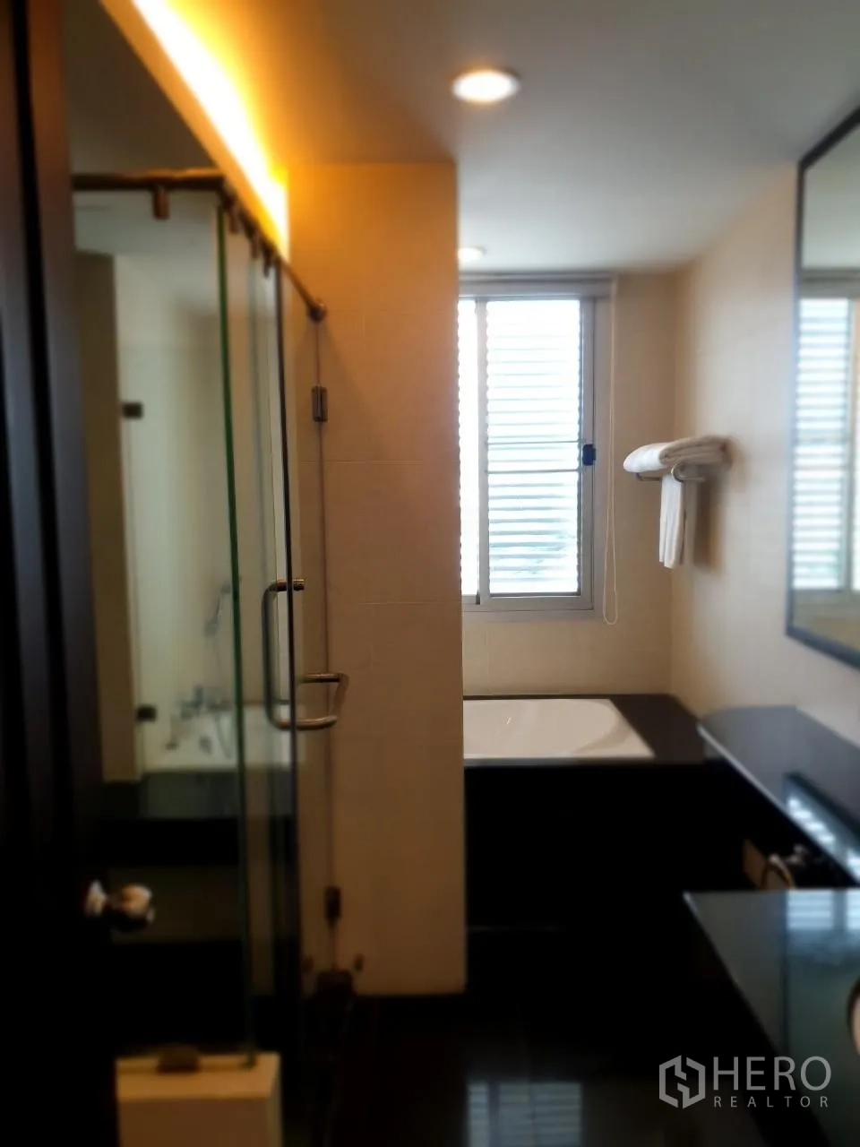 Apartment for rent in Bang Rak, Bangkok - Bathroom with glass shower, bathtub and natural-light window.