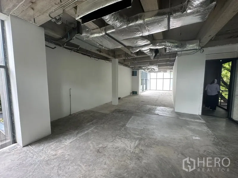 Office Space for rent in Khlong Toei, Bangkok - Open-plan office floor with exposed concrete ceiling, ductwork, white partition walls and large windows.