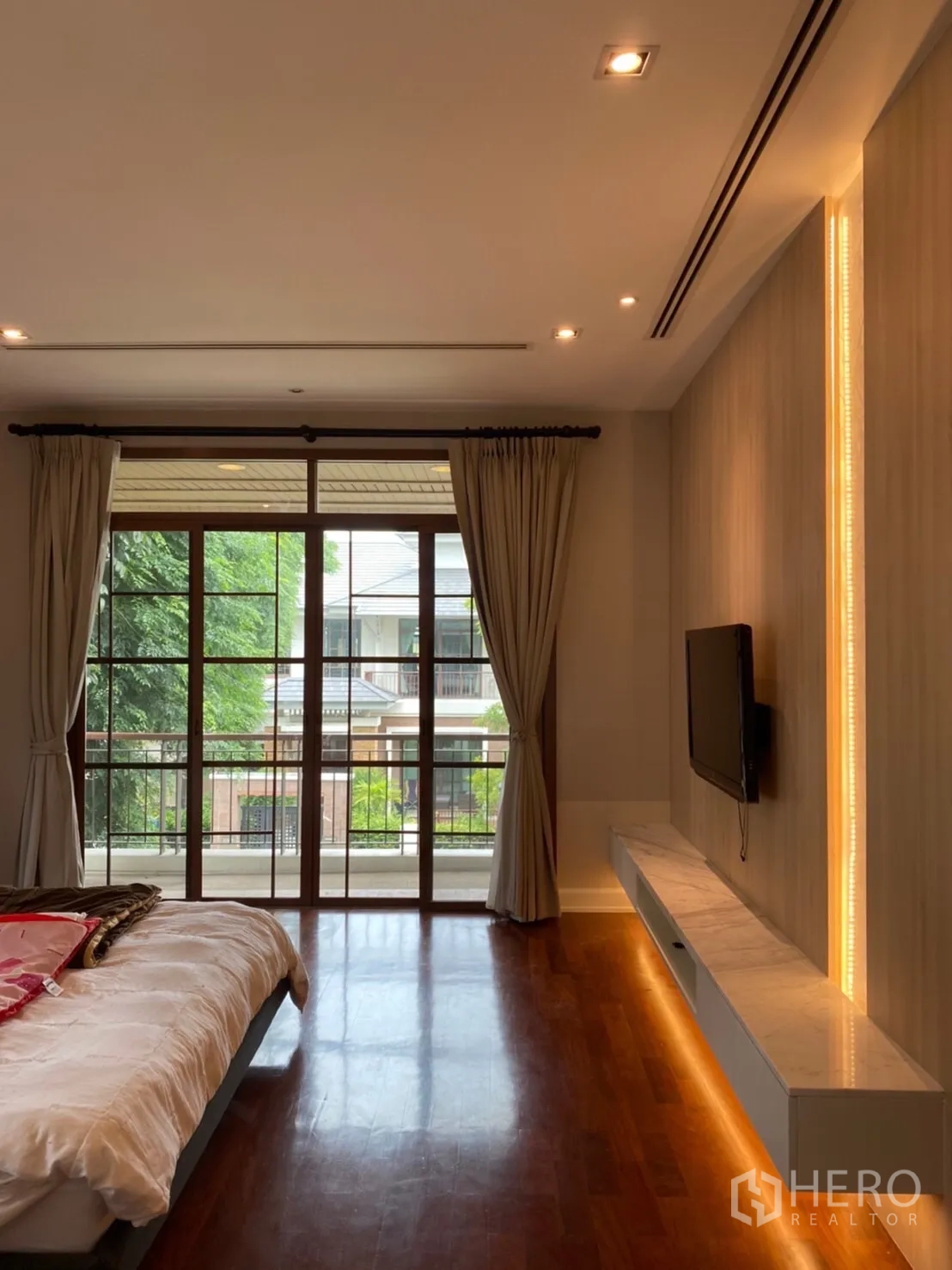 Detached House for rent in Bang Phli, Samut Prakan - Primary bedroom with wood floor, balcony doors and LED feature wall with mounted TV.
