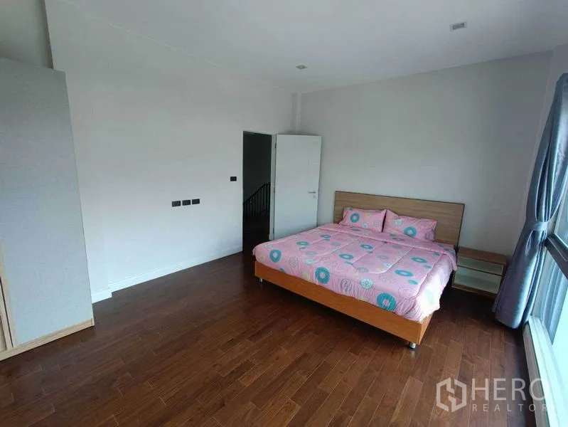 Detached House for rent in Bueng Kum, Bangkok - Secondary bedroom with wood floors, balcony-height window, and built-in side tables.
