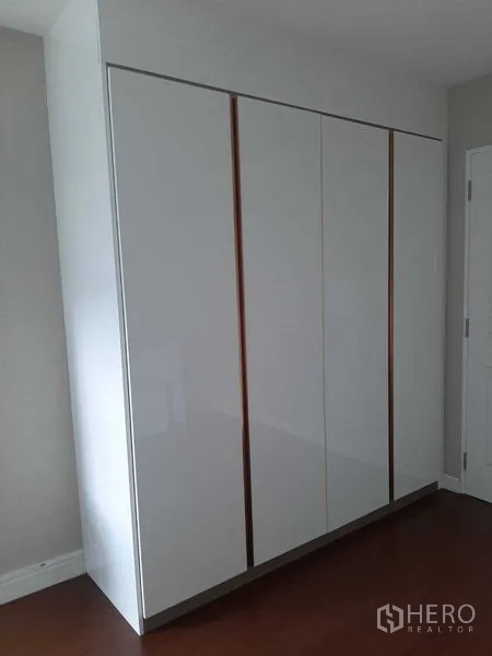 Condominium for rent or sale in Huai Khwang, Bangkok - Glossy white built-in wardrobe with four doors in a bedroom with wood floors