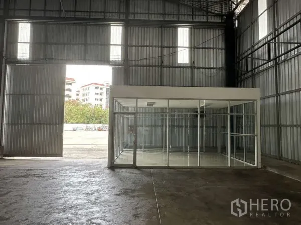 Warehouse for rent in Pak Kret, Nonthaburi - Interior entry showing tall sliding door and a glass-partition office facing the yard.