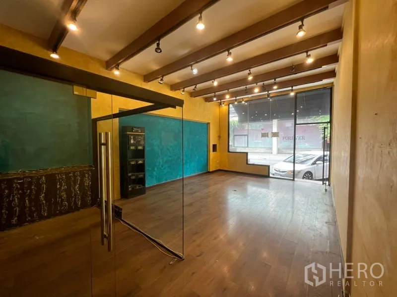 零售空间 出租在Watthana, Bangkok - 店内开放式空间，木地板、外露横梁、轨道灯与落地玻璃橱窗。