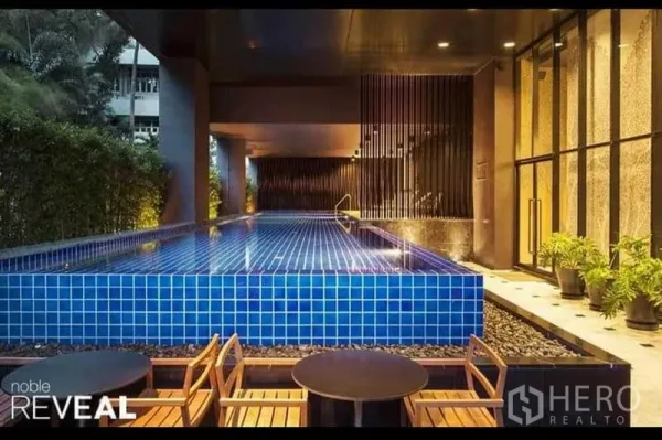 Condominium for rent or sale in Watthana, Bangkok - Condominium facility featuring a blue‑tiled swimming pool with seating area at dusk.