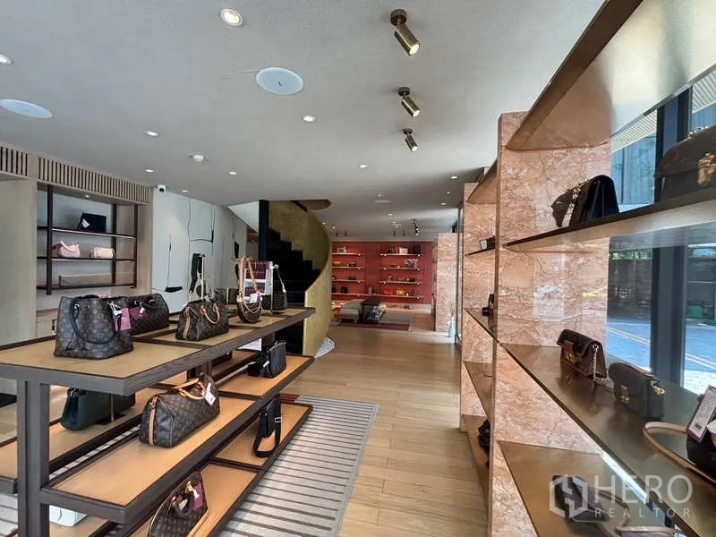 Retail Space for rent in Khlong Toei, Bangkok - Bright ground-floor retail showroom with wood flooring, open shelving and a spiral staircase.