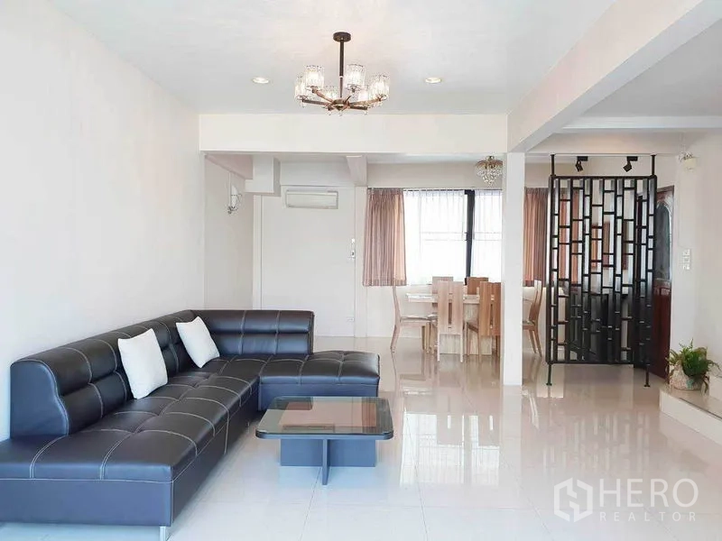 独立式住宅 出租在Phra Khanong, Bangkok - 宽敞客厅带吊灯，L型沙发与餐区相连。