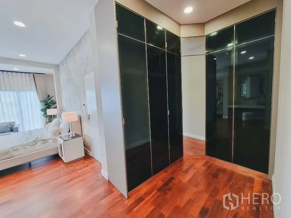Detached House for rent or sale in Bang Phli, Samut Prakan - Walk-in closet with glossy black wardrobes leading to a bedroom with wood floors.