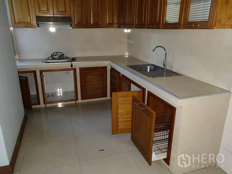 Home Office for rent in Watthana, Bangkok - L-shaped kitchen with gas hob, sink, and open storage cabinets.
