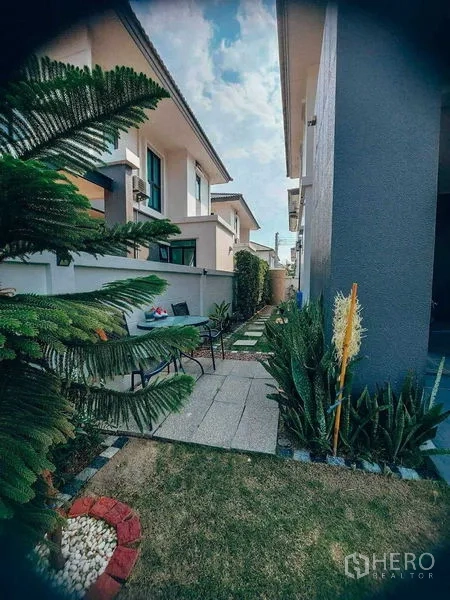 Detached House for rent in Bang Bo, Samut Prakan - Side yard walkway with outdoor seating, ferns and cactus plants along the wall.