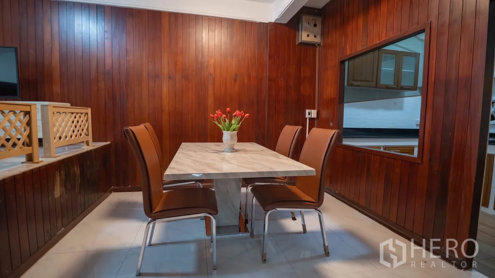 Townhouse for rent in Watthana, Bangkok - Dining area with a marble-top table and four chairs beside wood-paneled walls and a pass-through to the kitchen.