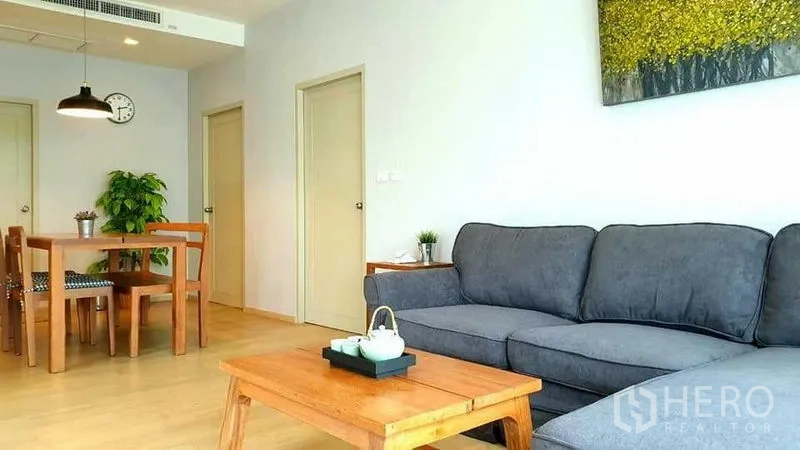 Condominium for rent or sale in Watthana, Bangkok - Bright living and dining area with grey sofa, wooden table set, light wood floors and a pendant light.