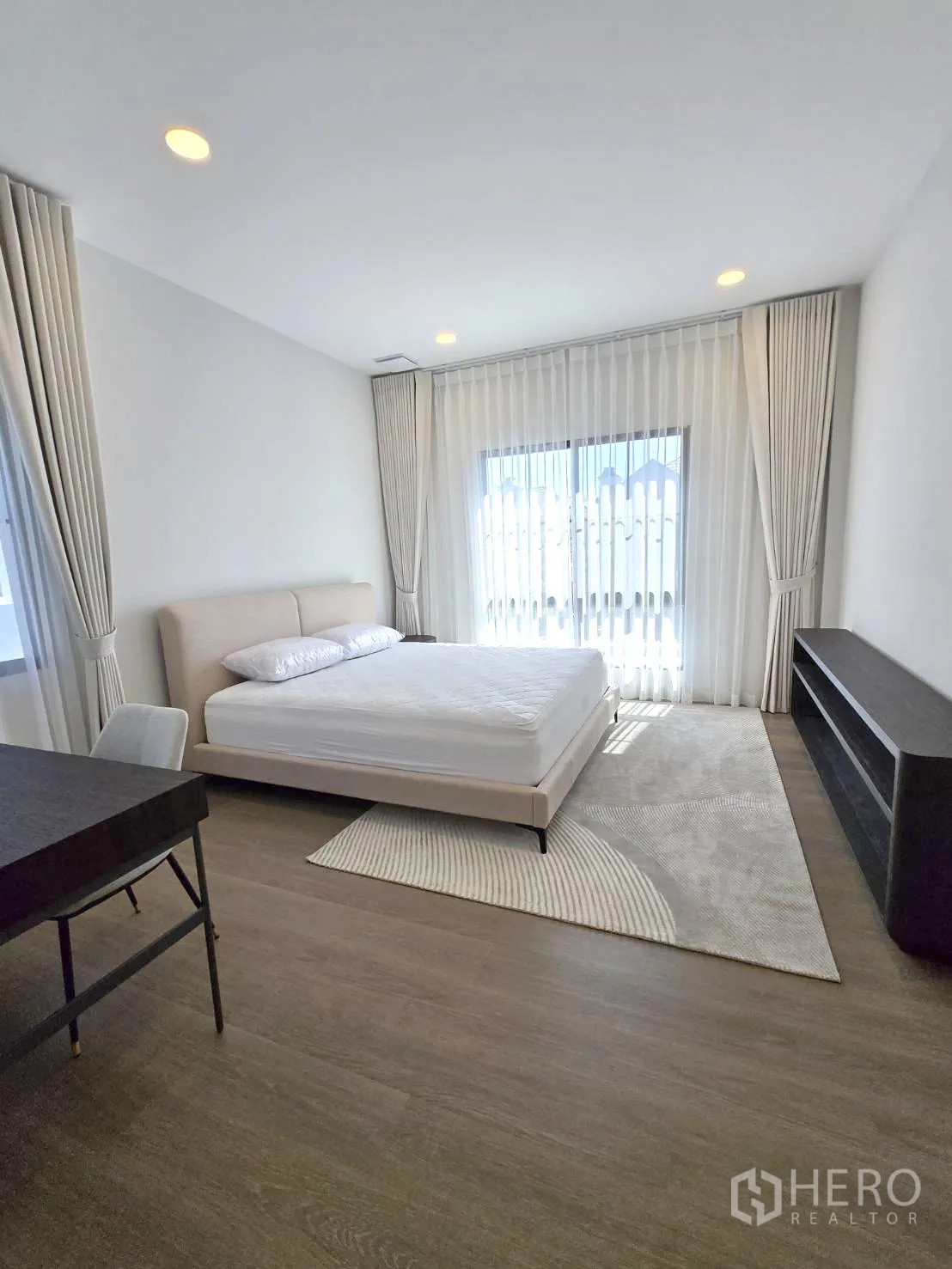 Detached House for rent in Saphan Sung, Bangkok - Bright bedroom with bed, writing desk and floor‑to‑ceiling drapes.