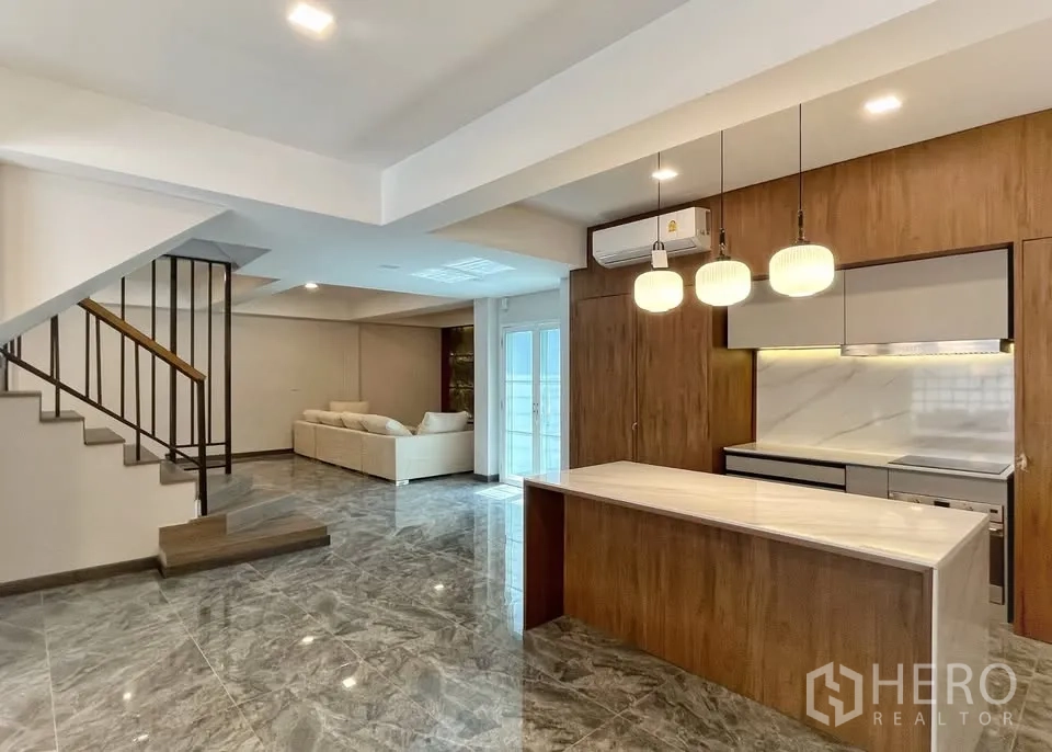 Home Office for rent in Watthana, Bangkok - Spacious living–dining room with island kitchen, sofa corner and metal stair railings.