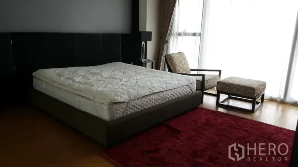 Condominium for rent in Sathon, Bangkok - Master bedroom with king bed, accent chair, red rug, and full-height windows for abundant light.