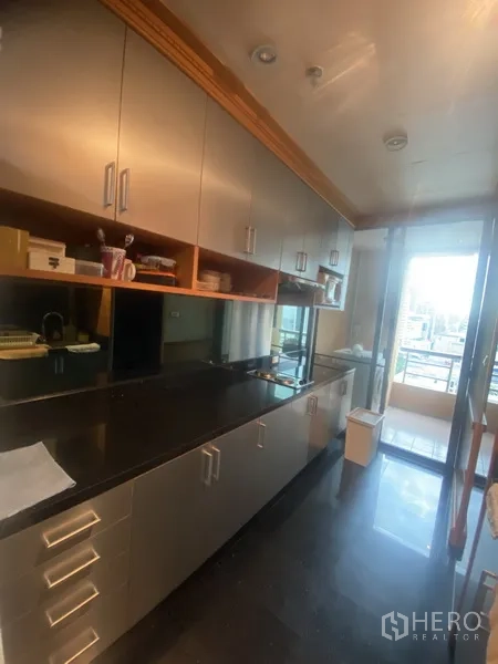Condominium for rent in Pathum Wan, Bangkok - Enclosed galley kitchen featuring stainless cabinetry, black countertops and a door to the balcony.