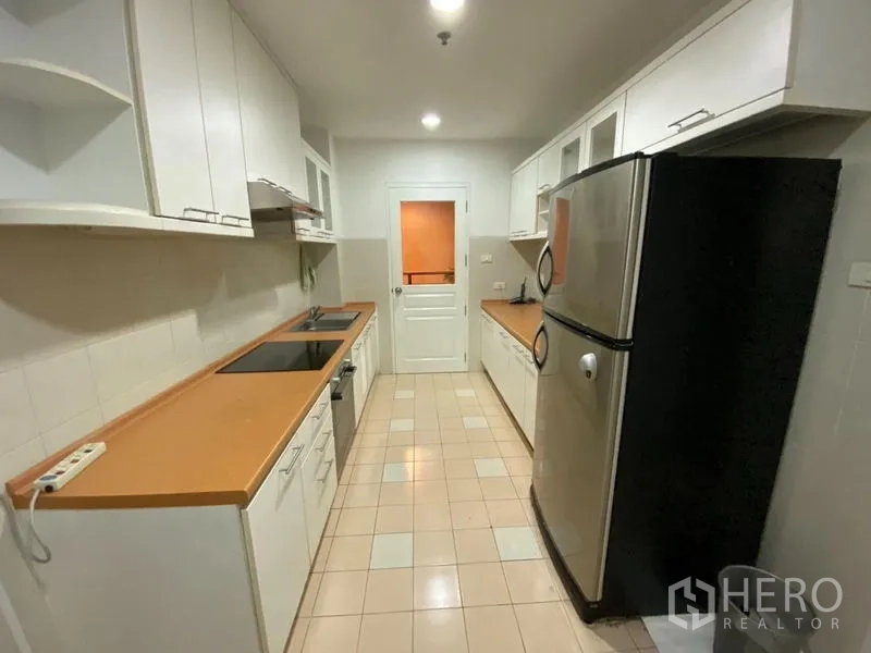 Condominium for rent in Pathum Wan, Bangkok - Galley kitchen with white cabinetry, electric hob, tiled floors and a stainless‑steel refrigerator.