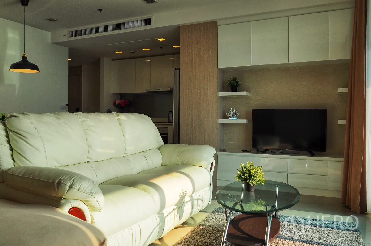 Condominium for rent in Bang Lamung, Chon Buri - Cozy living room with cream leather sofa, media wall and glass coffee table adjoining the fitted kitchen.