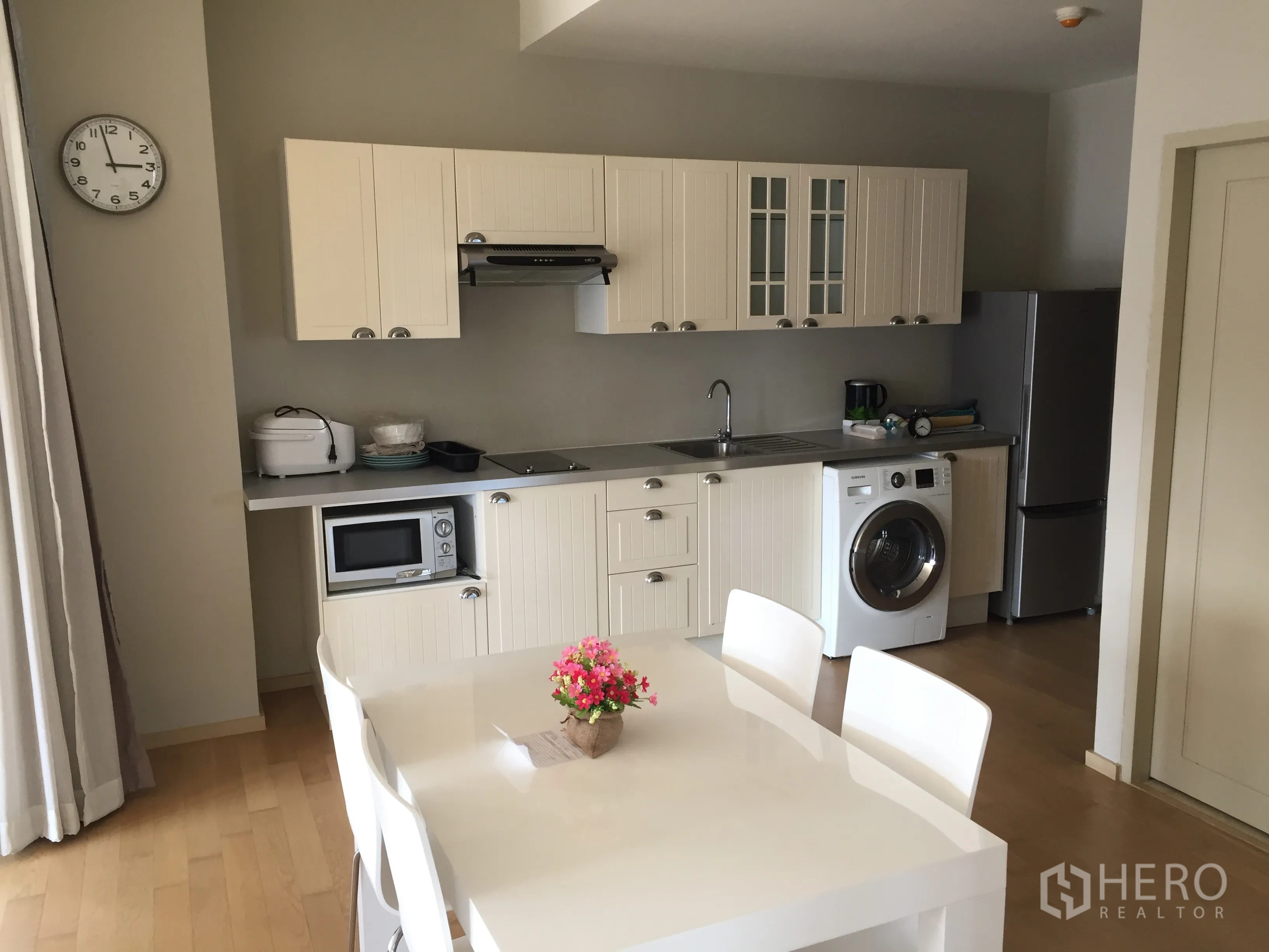 Condominium for rent or sale in Watthana, Bangkok - Open‑plan kitchen with white cabinetry, dining table, fridge, and washer in a 2‑bedroom condo.
