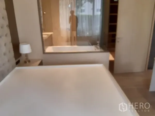 Condominium for rent or sale in Watthana, Bangkok - Bedroom with tufted headboard and glass wall opening to a bathroom with bathtub.