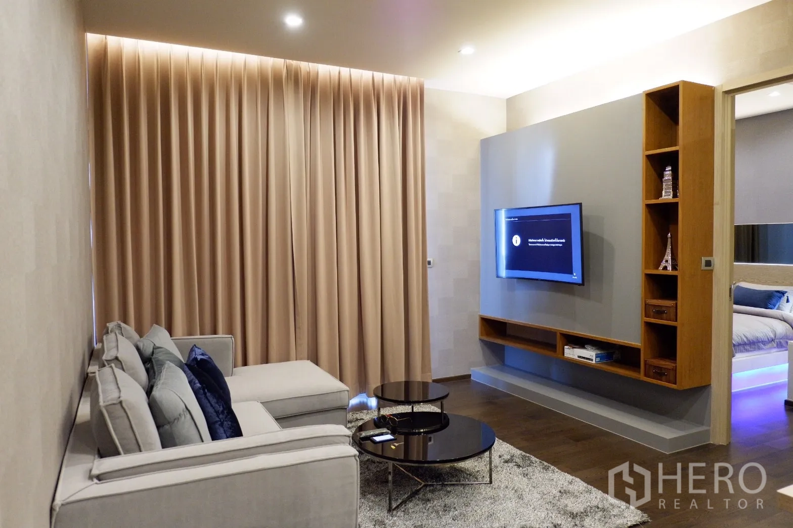 Condominium for rent in Watthana, Bangkok - Cozy living room with sectional sofa, wall-mounted TV and built-in shelving.