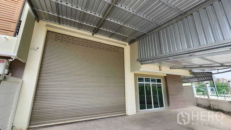Factory for rent in Samut Sakhon - Front loading area with large roller shutter door and glass entry.