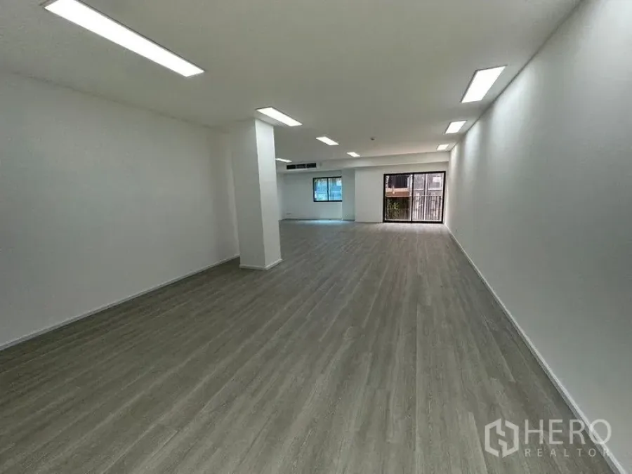 Office Space for rent - Spacious rectangular office with white walls, linear ceiling lights and wide-plank flooring leading to glass balcony doors.