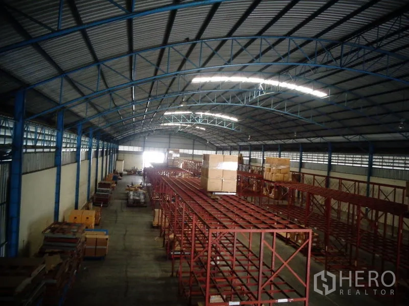 Warehouse for rent or sale in Lat Lum Kaeo, Pathum Thani - Panorama from mezzanine showing red racks, blue trusses and loading area at the far end.