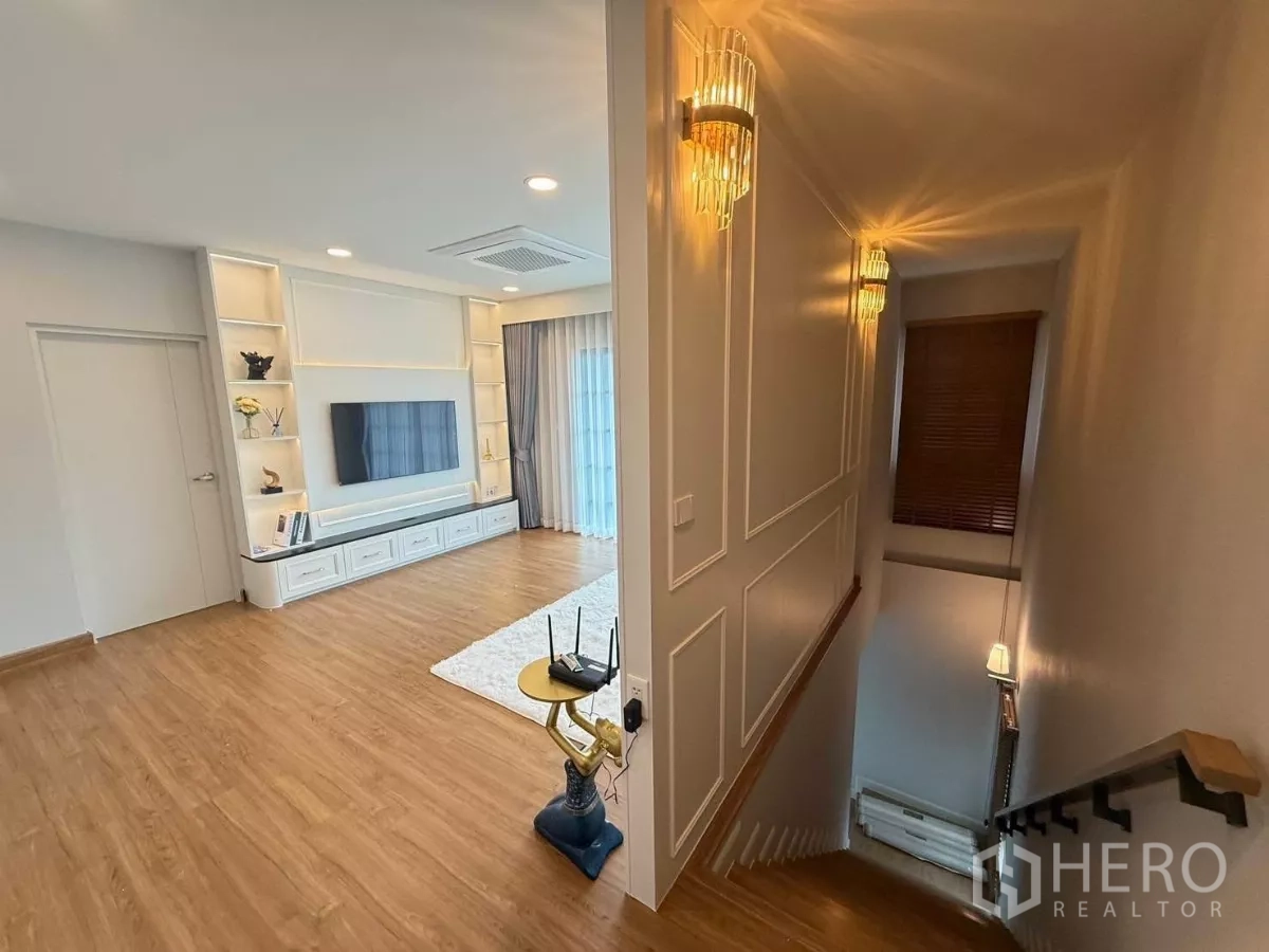 Detached House for rent in Bang Phli, Samut Prakan - Stair landing leading to an upstairs family room with wood flooring, TV wall and built-in shelving.