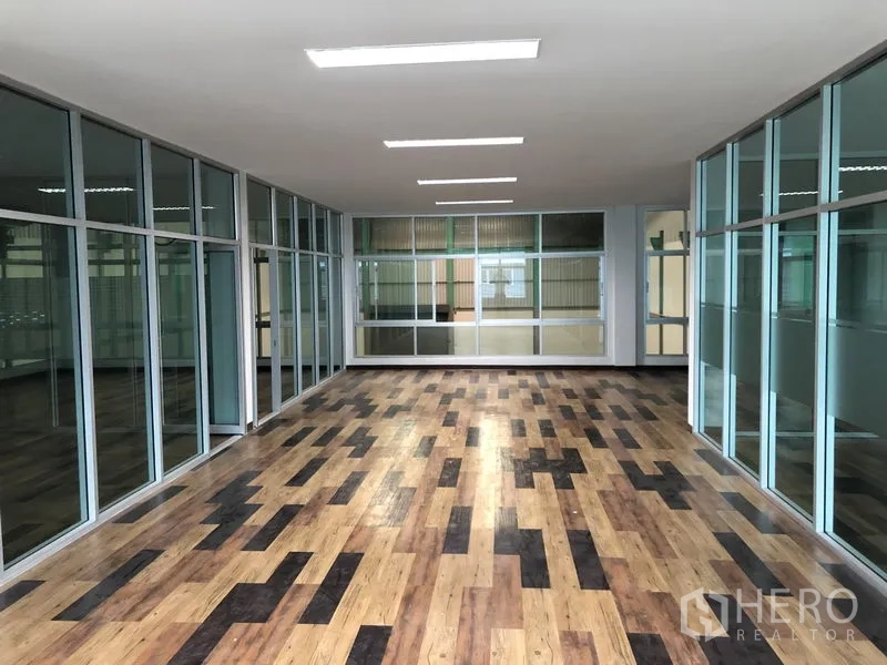 Factory for rent in Samut Prakan - Long office corridor with full‑height glass walls and wood‑pattern flooring.