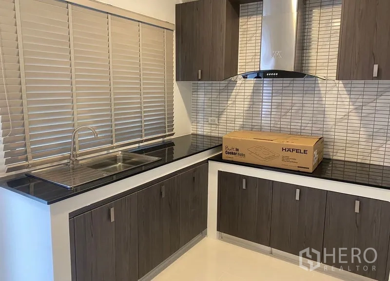 Detached House for rent in Bang Phli, Samut Prakan - Fitted kitchen with wood cabinets, tiled backsplash, sink and range hood.