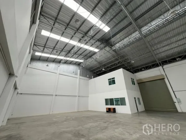 โรงงาน ให้เช่าในPhra Samut Chedi, Samut Prakan - มุมมองโกดังโล่งกว้าง พร้อมบล็อกออฟฟิศสีขาวภายใน หลังคาเหล็ก และประตูม้วนขนาดใหญ่