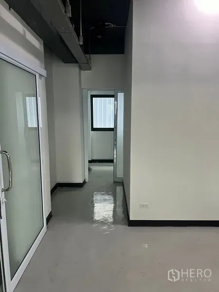 零售空间 出租在Watthana, Bangkok - 走廊与推拉玻璃入口，内有带窗的小型办公室。